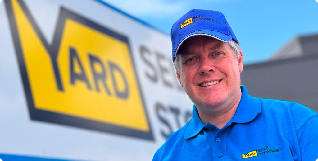 Yard Self-Storage director in front of their facility's sign.